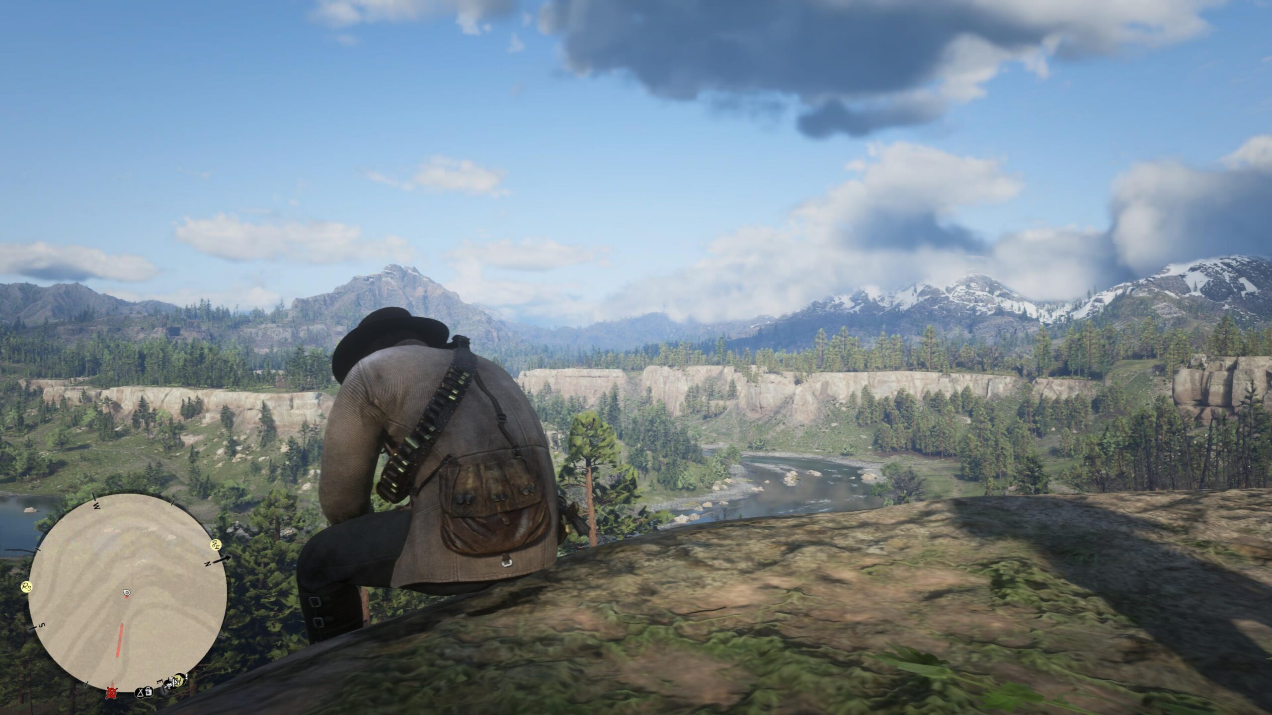 Arthur Morgan sitting on a rocky overlook in Red Dead Redemption 2, watching a river valley and snow-capped mountains