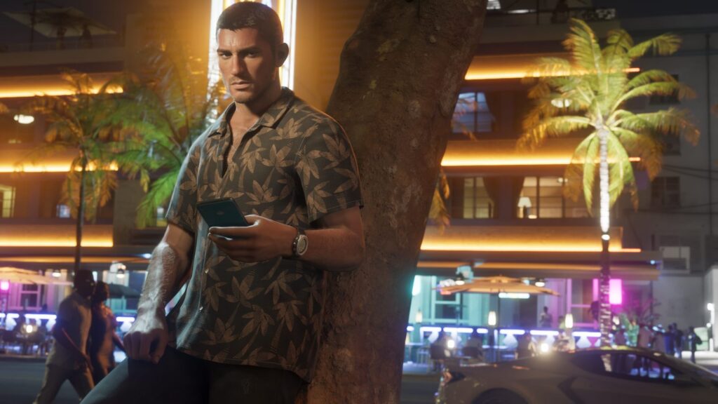 Jason standing under palm trees on a neon-lit Vice City street at night, looking at the phone in his hand. Image: Rockstar Games.