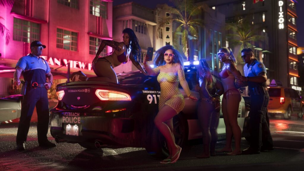 Vice Beach police officers standing beside a marked cruiser with its lights on outside a neon-lit Ocean View hotel at night, a crowd on the pavement. Image: Rockstar Games.