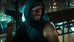 Jason in a white cap and hood carries a rifle under teal light. Image: Rockstar Games.