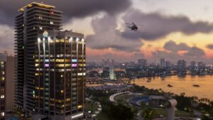 A Vice City tower block at dusk with the bay and marina beyond, a helicopter passing. Image: Rockstar Games.