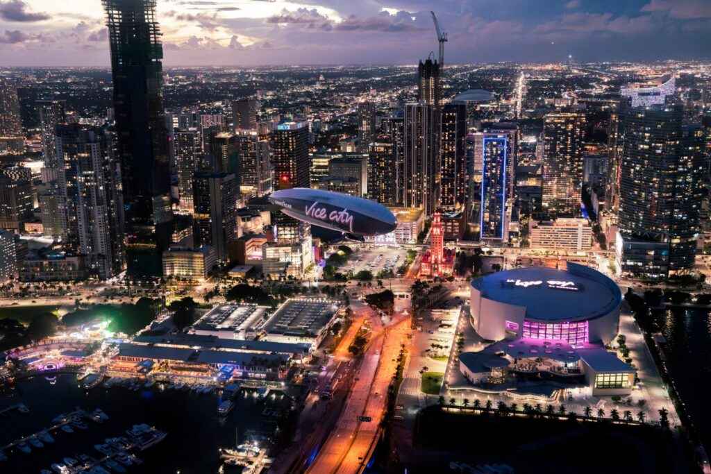 The Vice City Goodyear Blimp at night over downtown Miami, with the lit Kaseya Center arena and the Vice City lettering on its roof in the foreground. Image: Goodyear.